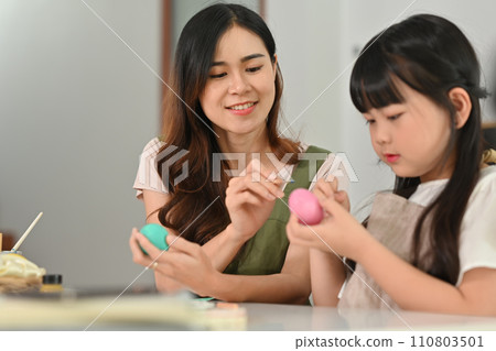 Smiling little girl painting Easter eggs with mother, getting ready for holiday at home Smiling little girl painting Easter eggs with mother, getting ready for holiday at home 110803501