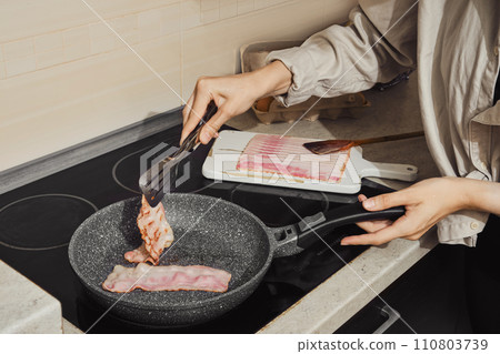 Hand of woman flipping bacon on frying pan Hand of woman flipping bacon on frying pan 110803739