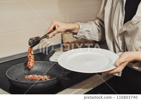 Unrecognizable woman removing fried bacon from a frying pan Unrecognizable woman removing fried bacon from a frying pan 110803740