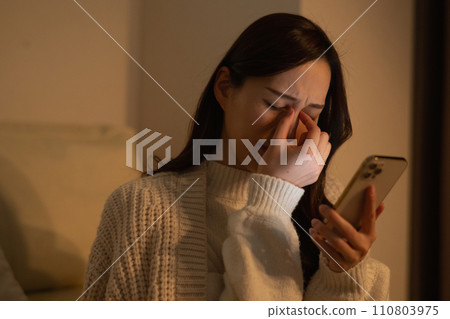 一位女士因深夜在黑暗的房間裡看智慧型手機而眼睛疲勞 110803975