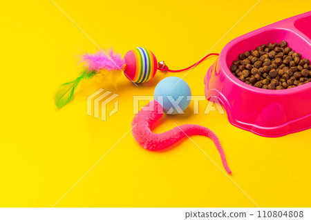 Cat bowl with dry food and toys on yellow background studio shot 110804808