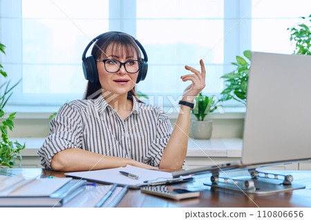 Middle-aged woman in headphones working at computer in home office Middle-aged woman in headphones working at computer in home office 110806656