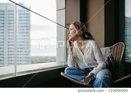 Female nurse or doctor enjoying free time at home after work, sitting by window listening meditation relaxing music. Work-life balance for healthcare worker. Female nurse or doctor enjoying free time at home after work, sitting by window listening meditation relaxing music. Work-life balance for healthcare worker. 110806900