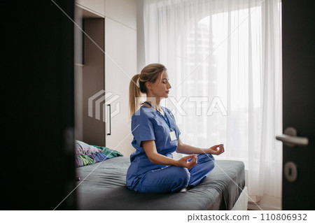Female nurse or doctor enjoying free time at home after work, meditating. Work-life balance for a healthcare worker. Female nurse or doctor enjoying free time at home after work, meditating. Work-life balance for a healthcare worker. 110806932