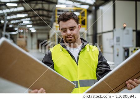 Portrait of young man with Down syndrome working in warehouse. Concept of workers with disabilities, support in workplace. Portrait of young man with Down syndrome working in warehouse. Concept of workers with disabilities, support in workplace. 110806945