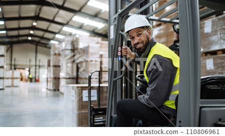 Portrait of warehouse worker driving forklift. Warehouse worker preparing products for shipmennt, delivery, checking stock in warehouse. Banner with copy space. Portrait of warehouse worker driving forklift. Warehouse worker preparing products for shipmennt, delivery, checking stock in warehouse. Banner with copy space. 110806961