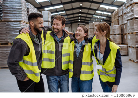 Full team of warehouse employees laughing in warehouse, holding each other by shoulders. Team of workers in reflective clothing in modern industrial factory, heavy industry, manufactrury. Full team of warehouse employees laughing in warehouse, holding each other by shoulders. Team of workers in reflective clothing in modern industrial factory, heavy industry, manufactrury. 110806969