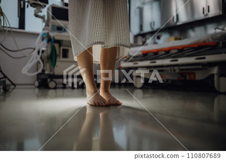 Close up of barefoot legs of patient, standing by hospital bed in emergency room. Anxiety, worry and loneliness of patient in hospital. 110807689