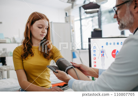 Doctor examining teenage girl, measuring blood pressure, using clinical blood pressure monitor. Concept of preventive health care for teenagers 110807705