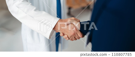Close up of pharmaceutical sales representative shaking hands with doctor in medical building. Doctor greeting hospital director, manager in private clinic. Banner with copy space. 110807785