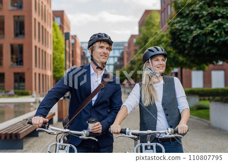 Spouses commuting through the city, talking and walking by bike on street. Middle-aged city commuters traveling from work by bike after a long workday. 110807795