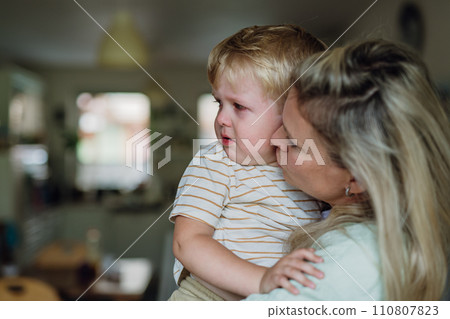 Mother calming little son, holding him, kissing on cheek. Boy is sad, crying. 110807823
