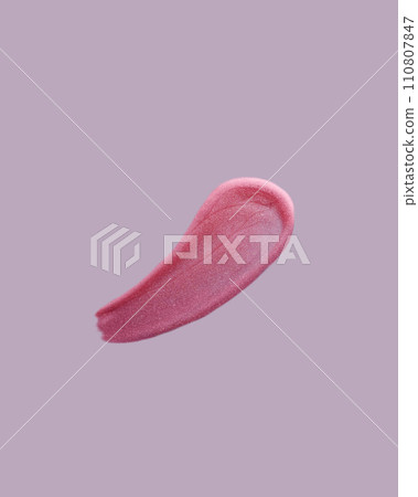 Pink shimmering lip gloss swatch texture on purple background. Lipstick smudged cosmetic product. Pink shimmering lip gloss swatch texture on purple background. Lipstick smudged cosmetic product. 110807847