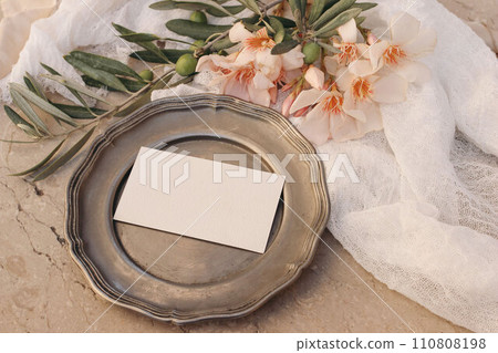 Summer stationery, branding mockup. Blank business, RSVP card, invitation. Vintage silver plate. Apricot oleander blossoms, ribbon and olive tree branches. Beige marble background. Flat lay, top view. Summer stationery, branding mockup. Blank business, RSVP card, invitation. Vintage silver plate. Apricot oleander blossoms, ribbon and olive tree branches. Beige marble background. Flat lay, top view. 110808198