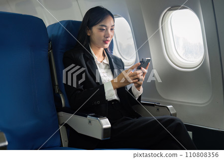 Beautiful Asian businesswoman using mobile phone in aeroplane. working, travel, business concept Beautiful Asian businesswoman using mobile phone in aeroplane. working, travel, business concept 110808356