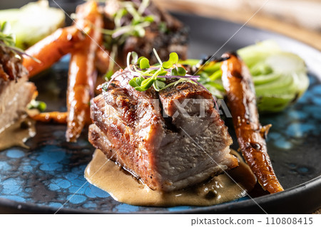Three pieces of baked belly with grilled vegetables on a plate in a pub or restaurant Three pieces of baked belly with grilled vegetables on a plate in a pub or restaurant 110808415
