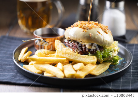 Beef burger topped with cheese with fries and draft beer on a pub or restaurant plate Beef burger topped with cheese with fries and draft beer on a pub or restaurant plate 110808445
