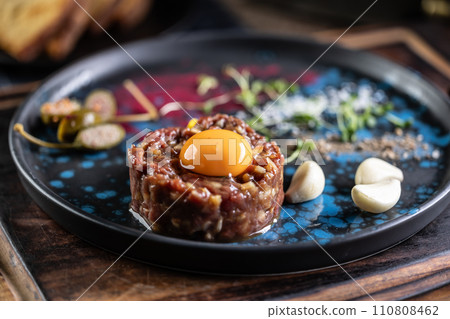Beef tartare with egg yolk on a plate with garlic and toasted bread 110808462