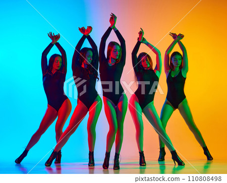 Artistic, expressive young women in black bodysuits dancing on high heels against gradient blue yellow background in neon light 110808498
