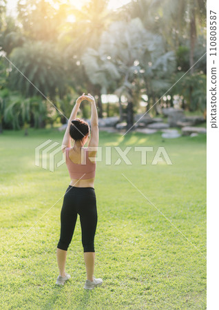 Back portrait of a 30s Asian woman, wearing pink sportswear, preparing her body and breathing fresh air before a sunset run in a public park. Embrace a wellness lifestyle and fitness outside. 110808587