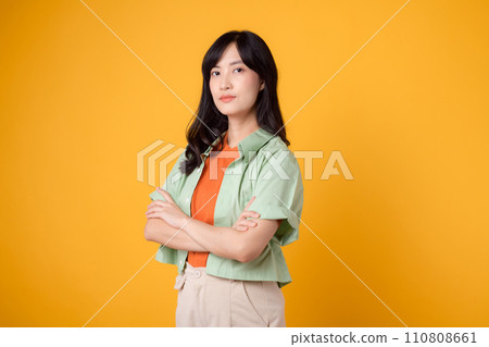 Radiate confidence portrait of young Asian woman wears pastel green shirt on orange shirt confidently crossing her arms. Perfect for capturing a sense of self assurance and empowerment. Radiate confidence portrait of young Asian woman wears pastel green shirt on orange shirt confidently crossing her arms. Perfect for capturing a sense of self assurance and empowerment. 110808661