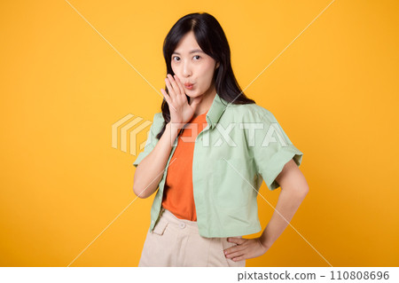 Capture young Asian woman 30s wearing a green shirt on an orange background, enthusiastically shouting with excitement. Explore the concept of discount shopping promotion with this vibrant image. 110808696
