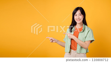 young Asian woman in her 30s wearing a green shirt on an orange shirt, pointing fingers to free copy space. Explore the concept of discount shopping promotion 110808712