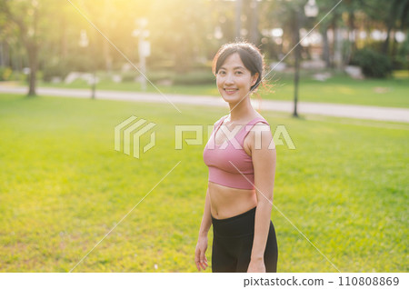 Experience the joy of a happy, fit female jogger in her 30s. Asian woman wearing pink sportswear, enjoying fresh air in a public park. Embrace wellness living and connect with nature. Experience the joy of a happy, fit female jogger in her 30s. Asian woman wearing pink sportswear, enjoying fresh air in a public park. Embrace wellness living and connect with nature. 110808869