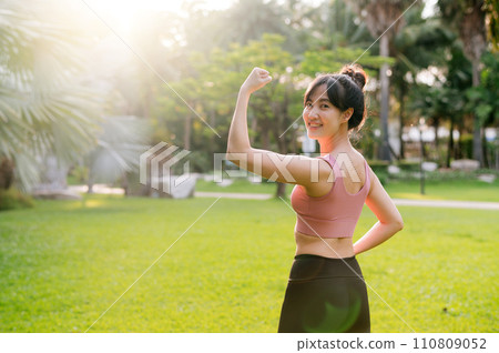 strength female jogger, fit 30s young Asian woman wearing pink sportswear, showing powerful body in park. healthy outdoor lifestyle fitness runner girl, at sunrise. wellness and well-being concept. strength female jogger, fit 30s young Asian woman wearing pink sportswear, showing powerful body in park. healthy outdoor lifestyle fitness runner girl, at sunrise. wellness and well-being concept. 110809052