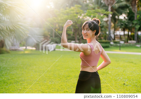 strength female jogger, fit young Asian woman 30s wearing pink sportswear, showing powerful body in park. healthy outdoor lifestyle fitness runner girl, at sunset. wellness and well-being concept. 110809054