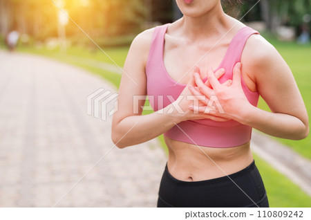 Woman jogger. young asian female wearing pink sportswear holding hands on chest after running in public park. Healthcare exercise pain concept. Woman jogger. young asian female wearing pink sportswear holding hands on chest after running in public park. Healthcare exercise pain concept. 110809242