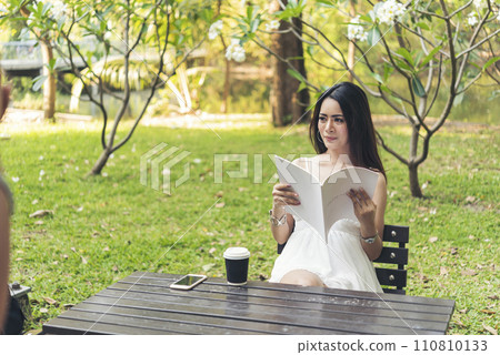 Asian woman holding book reading magazine at green park in natural garden. Young woman relaxation read open book self study. University women smiling with happiness learning. Women sit in green park Asian woman holding book reading magazine at green park in natural garden. Young woman relaxation read open book self study. University women smiling with happiness learning. Women sit in green park 110810133