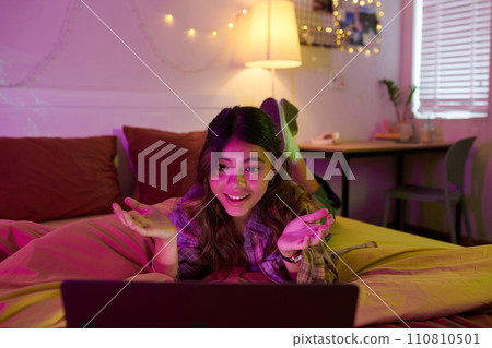 Excited girl lying on bed when video calling her best friend at night 110810501