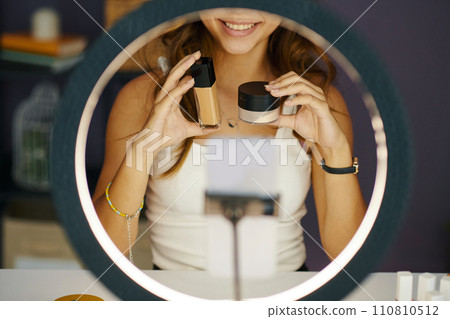 Smiling girl showing foundation and face powder to her subscribers when filming beauty blog 110810512