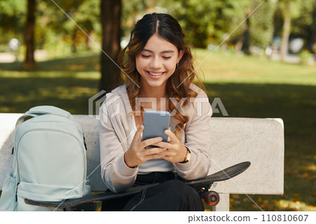 Cheerful teenage girl playing game on smartphone after school Cheerful teenage girl playing game on smartphone after school 110810607