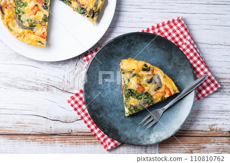 Italian Frittata made with spinach, tomatoes, onion and peppers on white wooden table Italian Frittata made with spinach, tomatoes, onion and peppers on white wooden table 110810762