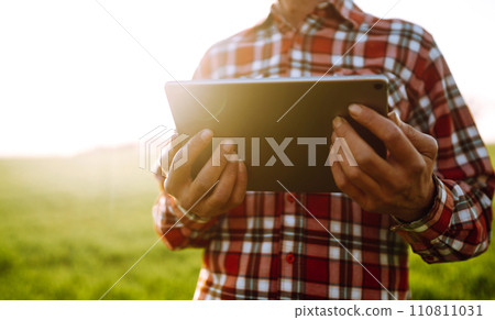 Tablet in the hands of a farmer. Smart farm. Farmer checking his crops on an agricultural field. 110811031