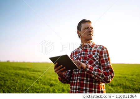 Farmer working with digital tablet in field at sunset. Checking wheat field. Agriculture concept. Farmer working with digital tablet in field at sunset. Checking wheat field. Agriculture concept. 110811064