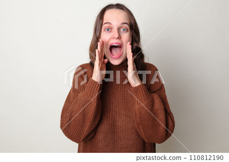Amazed Caucasian woman wearing brown jumper standing isolated over gray background screaming with hands near mouth making advertisement yelling loud announcing good important news Amazed Caucasian woman wearing brown jumper standing isolated over gray background screaming with hands near mouth making advertisement yelling loud announcing good important news 110812190