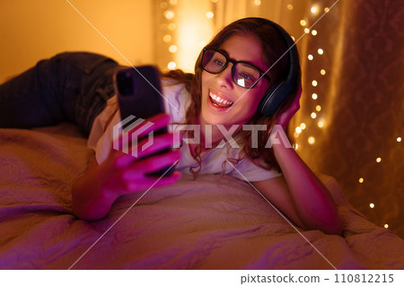 Woman communicates with friends on smartphone in headphones while sitting at home. Freelance concept 110812215