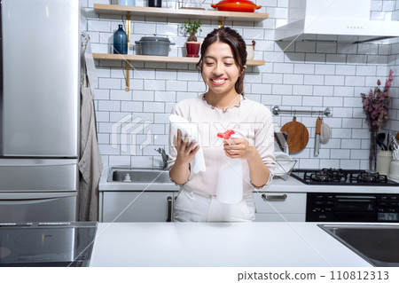 一名婦女在廚房的布上噴灑消毒劑 一名婦女在廚房的布上噴灑消毒劑 110812313