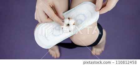 Sanitary napkin and cotton plant flower. The girl shows a cotton sanitary pad against the background of her panties. Concept of plastic-free products for women menstruation. Eco friendly products 110812458
