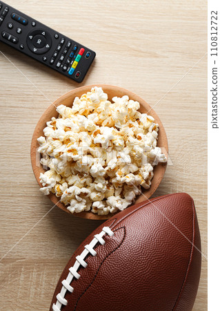 A bowl with popcorn, a rugby ball and a remote control A bowl with popcorn, a rugby ball and a remote control 110812722