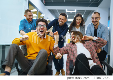 Young cheerful business people racing on office chairs and laughing. Funny activity Young cheerful business people racing on office chairs and laughing. Funny activity 110812850