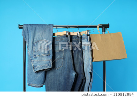 Ukraine, Kyiv, 28.10.2023 Jeans hang on hangers on a blue background Ukraine, Kyiv, 28.10.2023 Jeans hang on hangers on a blue background 110812994