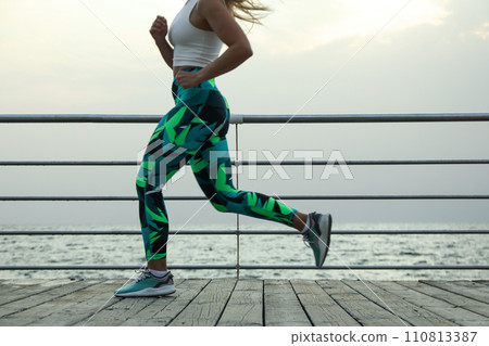 Young woman in sportswear runs along sea Young woman in sportswear runs along sea 110813387