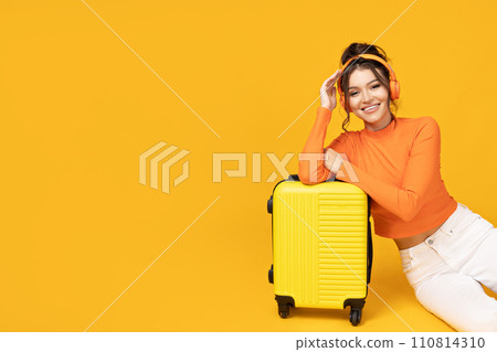 A young girl in headphones and with a yellow suitcase A young girl in headphones and with a yellow suitcase 110814310