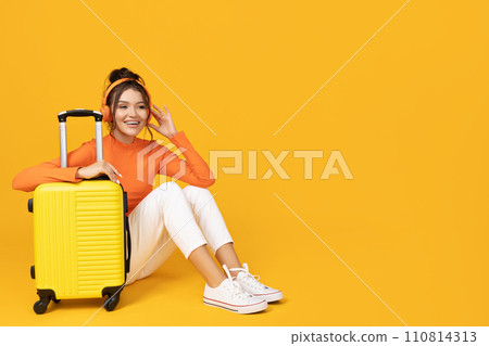 A young girl in headphones and with a yellow suitcase 110814313