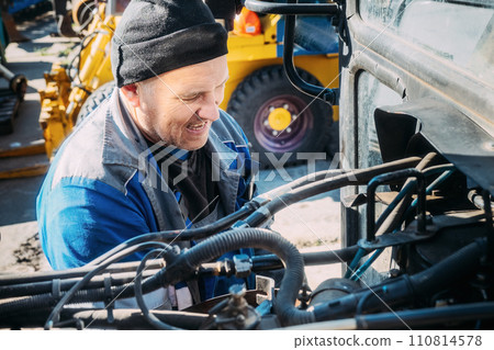 Mechanic repairs engine of tractor or heavy equipment. Farmer inspects and diagnoses agricultural Mechanic repairs engine of tractor or heavy equipment. Farmer inspects and diagnoses agricultural 110814578