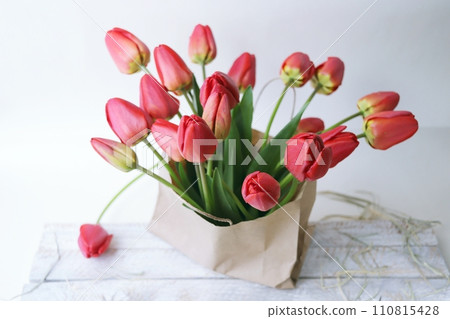 Bouquet of blooming red tulips in a paper bag on a white background, spring flowers 110815428